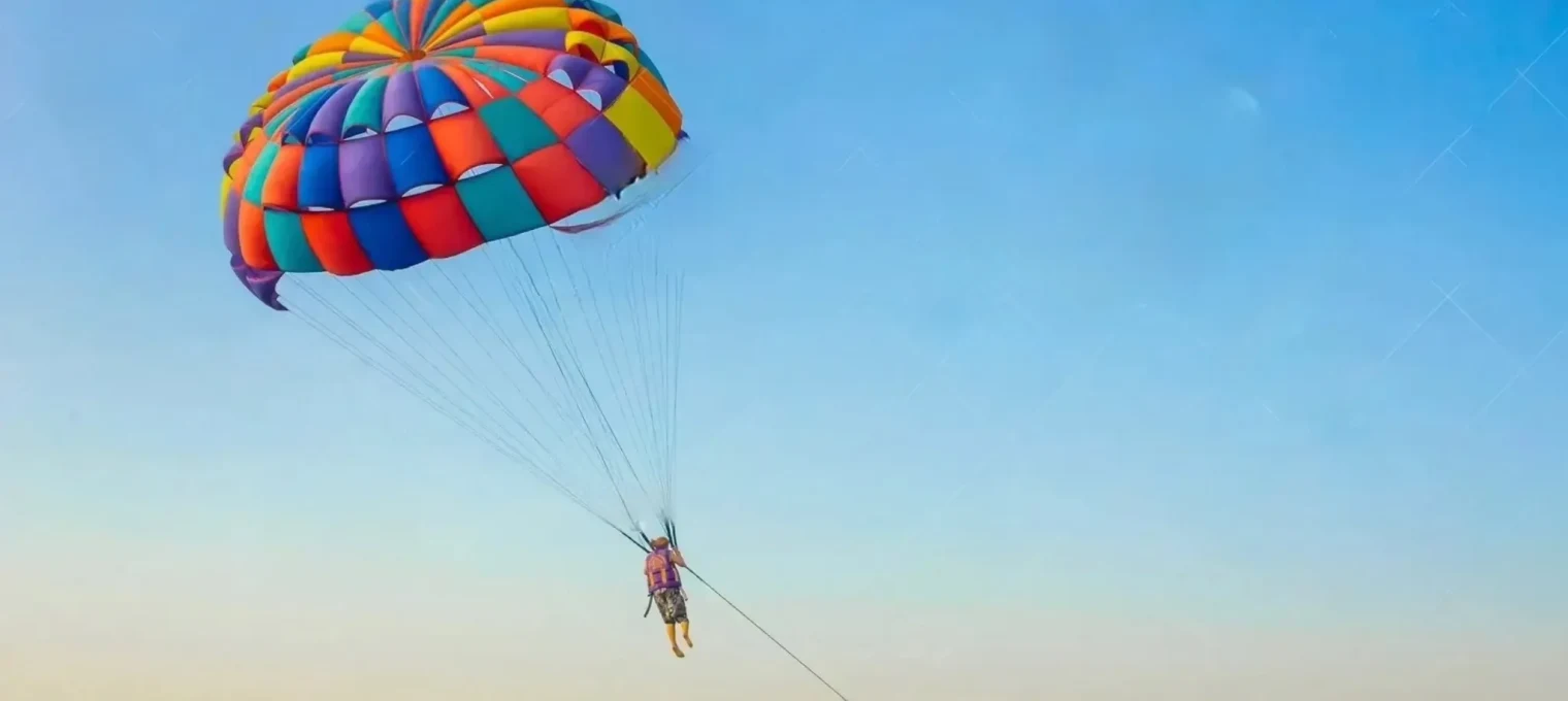 Person paragliding with a colorful parachute over a clear blue sky in Phuket.