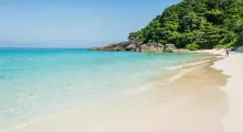 Serene beach scene in Phuket, featuring clear turquoise waters and lush greenery.
