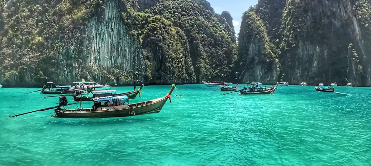 Colorful longtail boats in turquoise water surrounded by lush cliffs in Phuket.