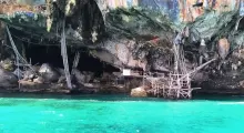 Bamboo structures beside turquoise waters under a rocky cliff in Phuket, Thailand.