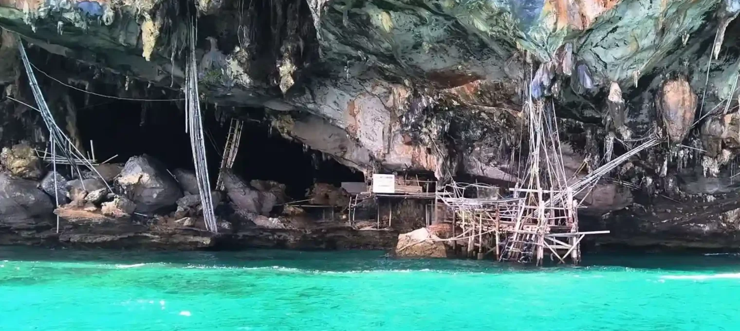 Bamboo structures beside turquoise waters under a rocky cliff in Phuket, Thailand.