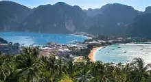 Scenic view of Phuket's coastline with lush palm trees, mountains, and clear blue waters.
