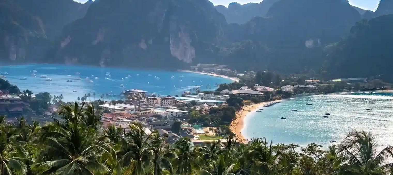 Scenic view of Phuket's coastline with lush palm trees, mountains, and clear blue waters.