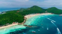Aerial view of boats on turquoise waters near lush green hills in Phuket, Thailand.