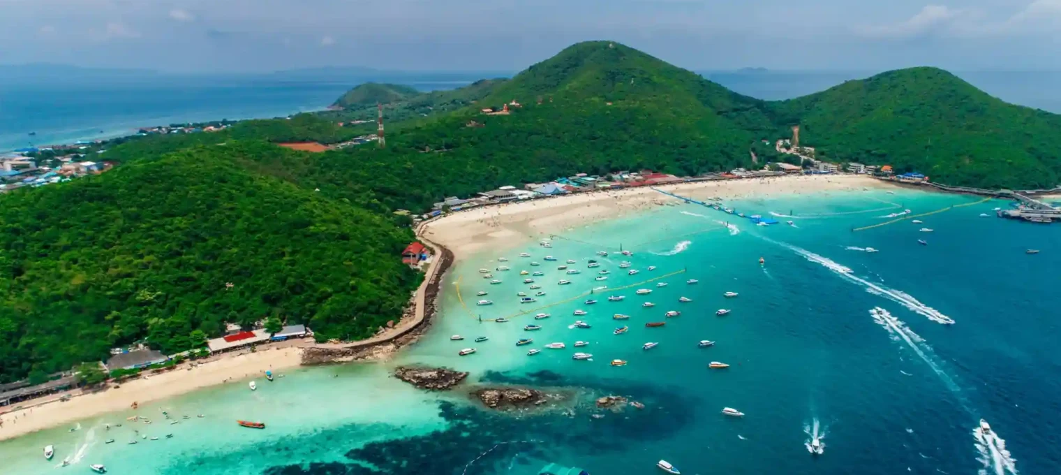 Aerial view of boats on turquoise waters near lush green hills in Phuket, Thailand.