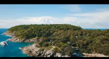 Aerial view of a lush green island with rocky shores in Phuket, Thailand.