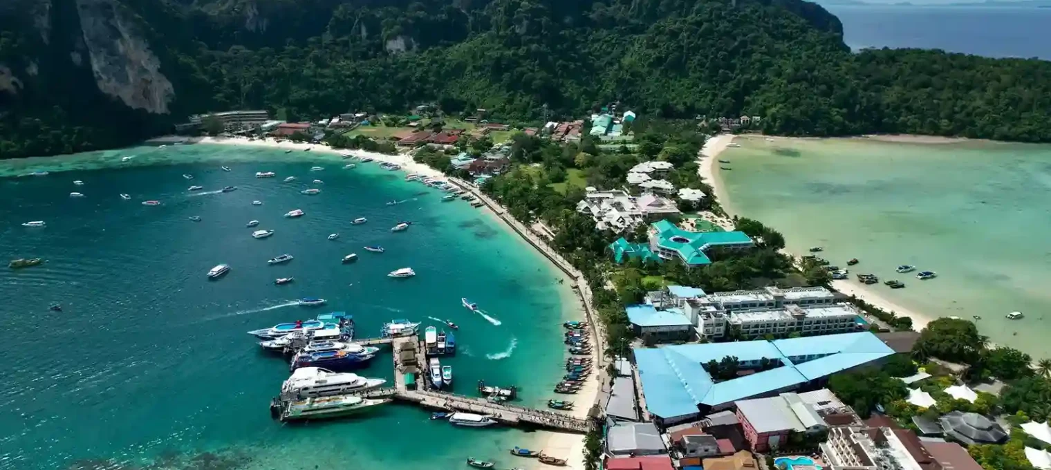Aerial view of Phuket's coastline with boats, lush hills, and sandy beaches.
