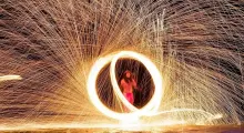 Fire performer creating a circular spark display at night on a beach in Phuket.