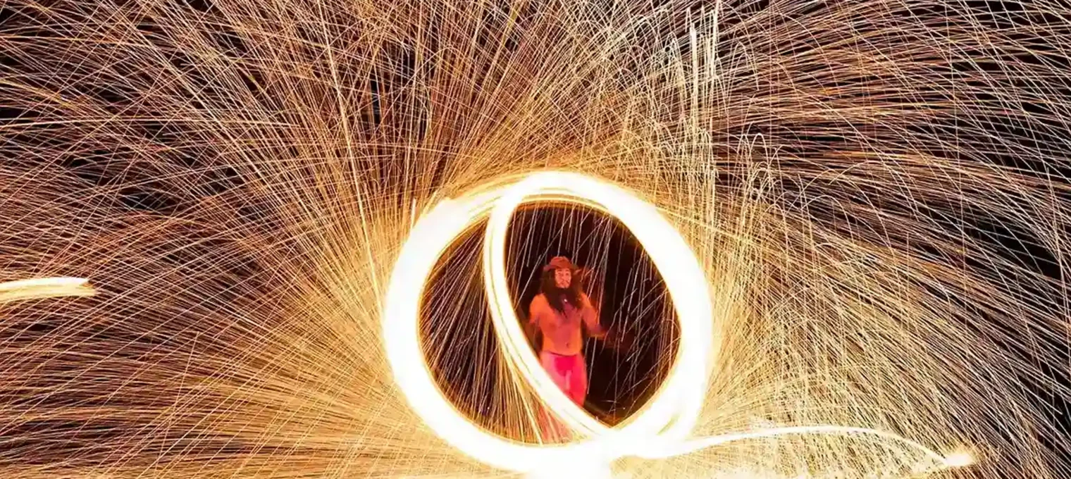 Fire performer creating a circular spark display at night on a beach in Phuket.