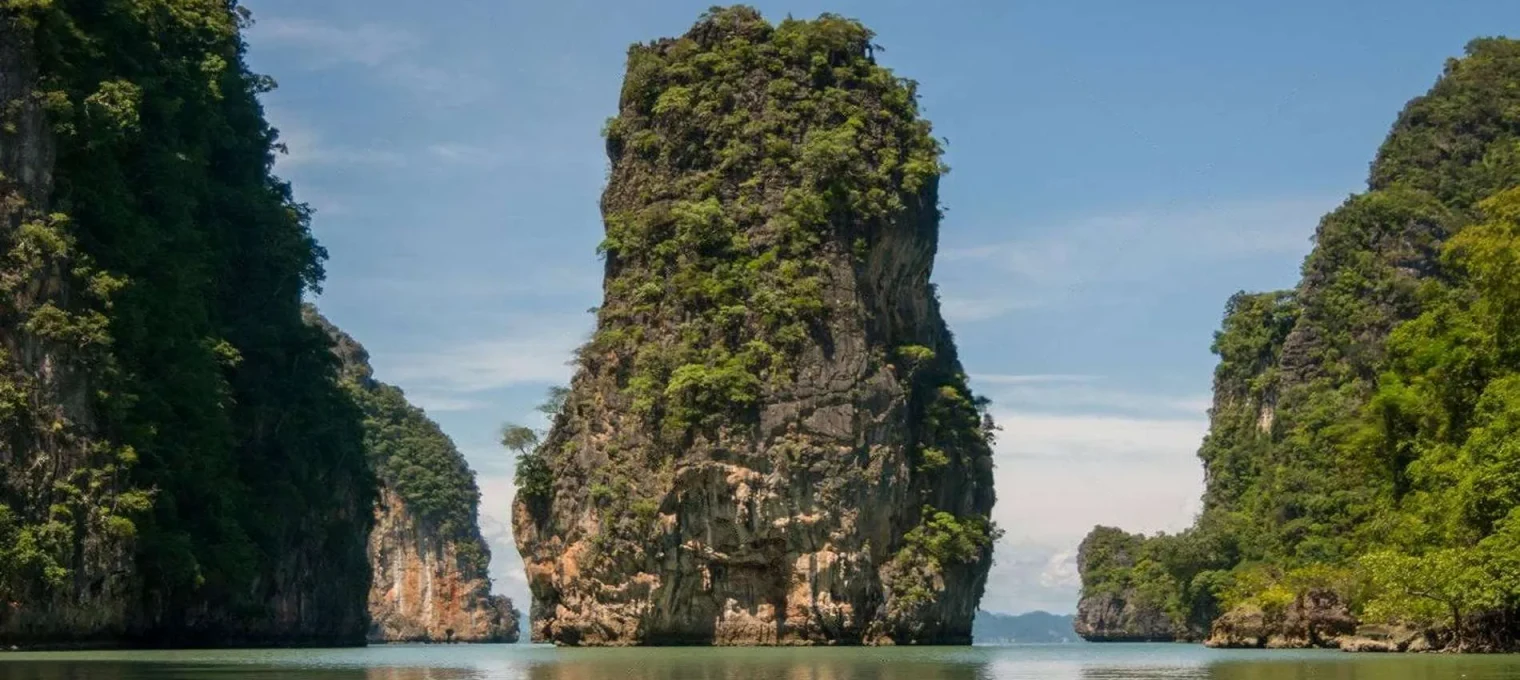 Stunning limestone cliffs rise from calm waters in Phuket, lush greenery adorning the peaks.