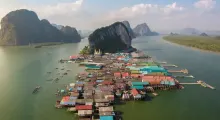 Aerial view of colorful stilt houses on water in Phuket, surrounded by lush mountains.