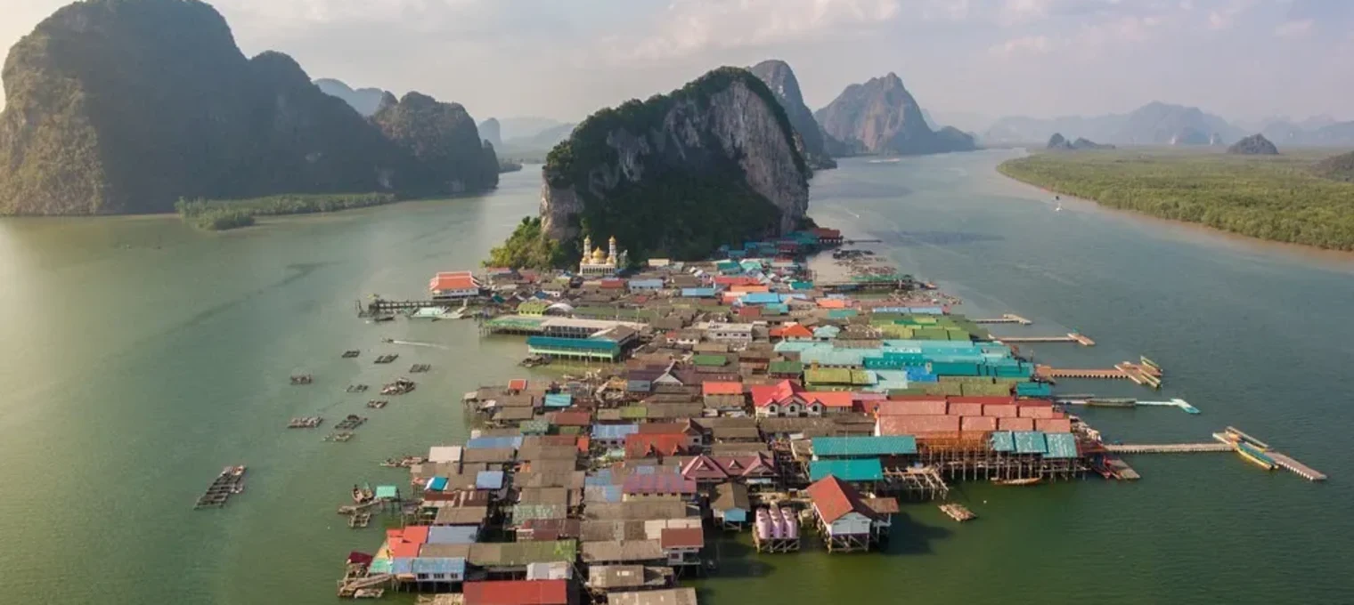 Aerial view of colorful stilt houses on water in Phuket, surrounded by lush mountains.