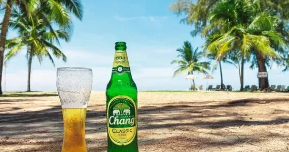 Стеклянный стакан с пивом Chang и бутылка на пляже в Пхукете, окруженные пальмами.