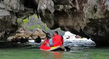 A couple in a kayak paddles through a rocky cave in Phuket, surrounded by green waters.