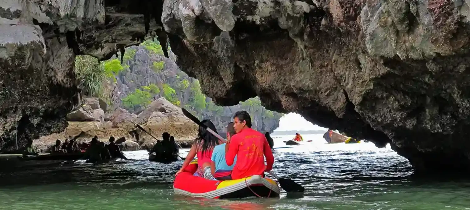 A couple in a kayak paddles through a rocky cave in Phuket, surrounded by green waters.