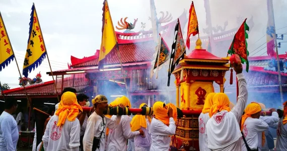 Participants in traditional festival carry a decorated shrine amidst smoke and colorful flags in Phuket.