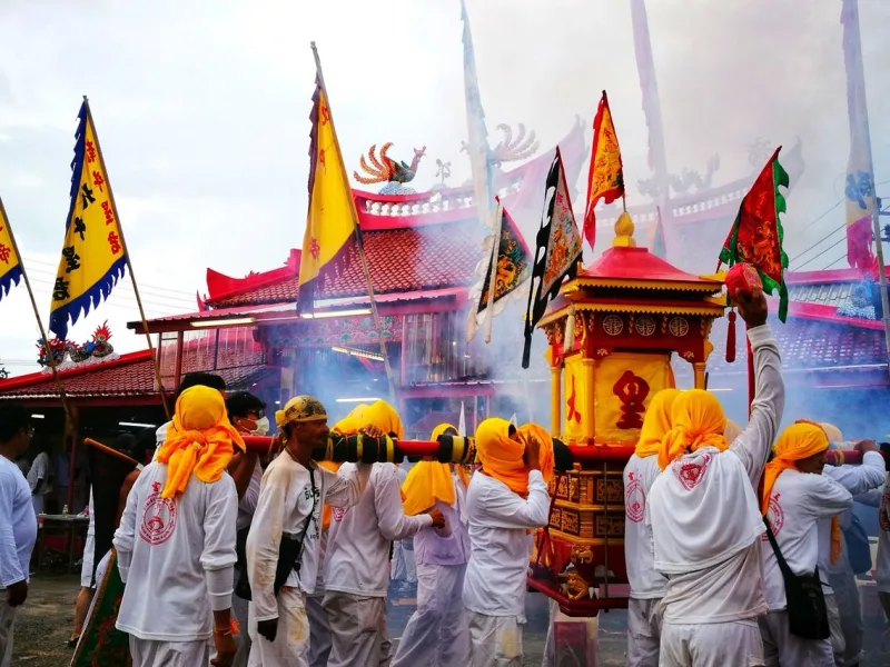 Participants in traditional festival carry a decorated shrine amidst smoke and colorful flags in Phuket.