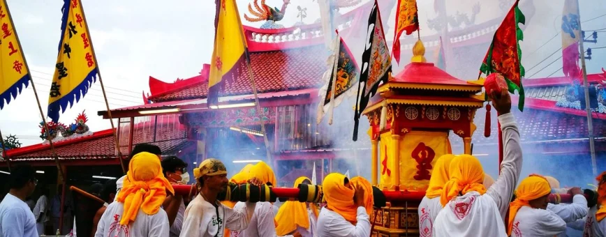 Participants in traditional festival carry a decorated shrine amidst smoke and colorful flags in Phuket.