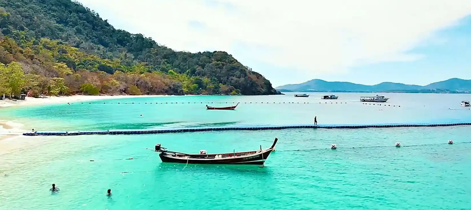 A serene beach scene in Phuket with turquoise waters and traditional boats.