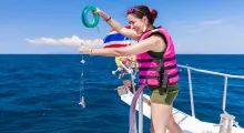Woman in a pink life jacket fishing from a boat in Phuket, with a bright blue sea backdrop.