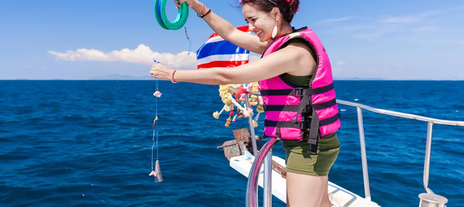 Woman in a pink life jacket fishing from a boat in Phuket, with a bright blue sea backdrop.