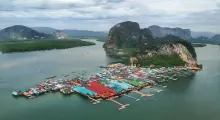 Colorful stilt houses on water in Phuket, surrounded by lush mountains and calm waters.