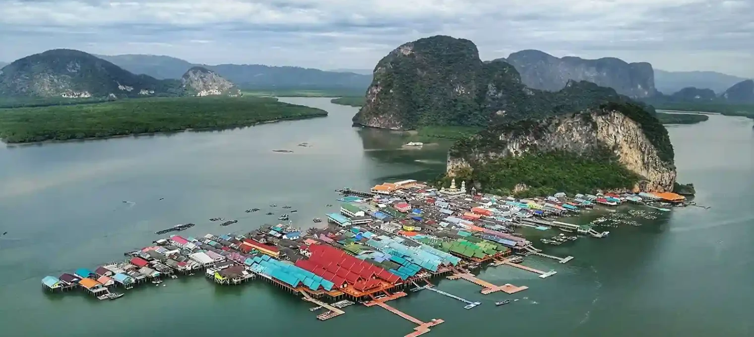 Colorful stilt houses on water in Phuket, surrounded by lush mountains and calm waters.