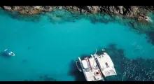 Aerial view of a boat anchored in crystal-clear turquoise waters near rocky coastline in Phuket.