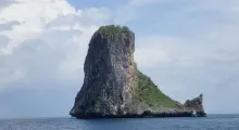 Lone rock formation surrounded by calm sea, with greenery atop, near Phuket.