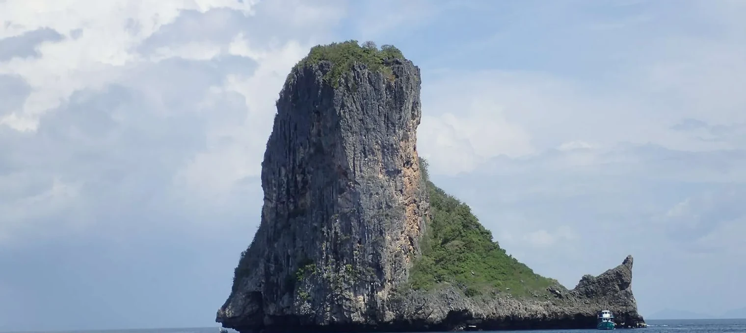 Lone rock formation surrounded by calm sea, with greenery atop, near Phuket.