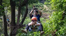 Two men ziplining through lush greenery in Phuket, Thailand. One is in front, capturing the moment.