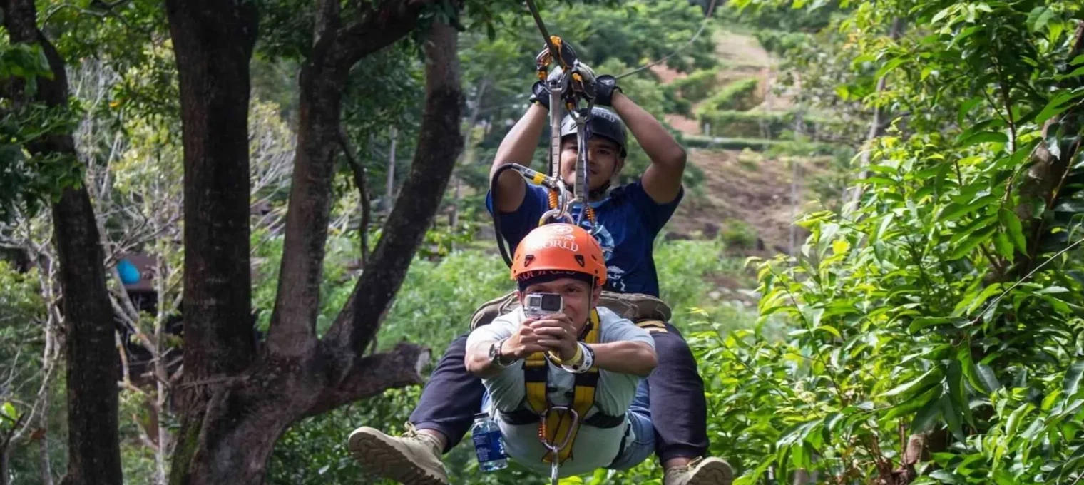 Two men ziplining through lush greenery in Phuket, Thailand. One is in front, capturing the moment.