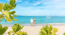 A couple standing on a beach in Phuket, gazing at the ocean under a blue sky.