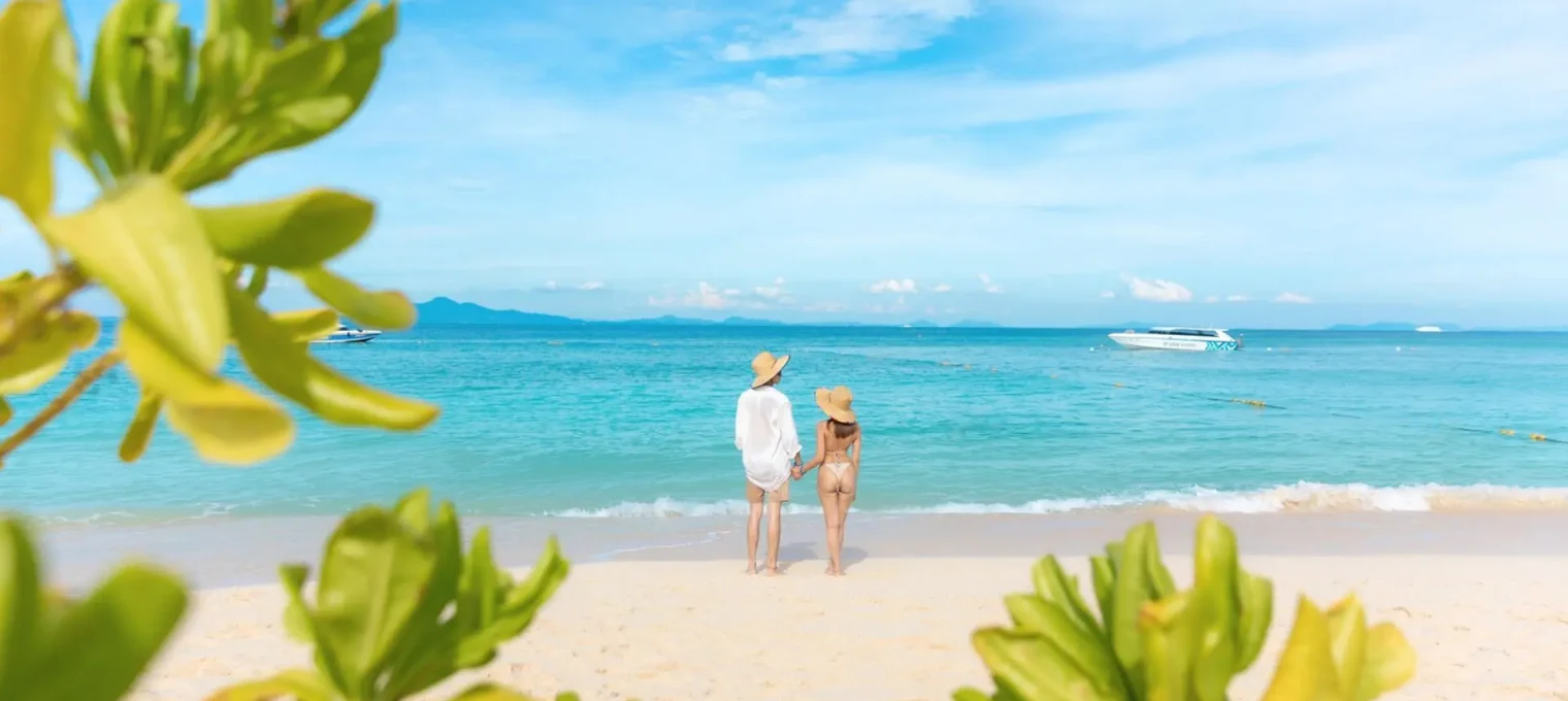 A couple standing on a beach in Phuket, gazing at the ocean under a blue sky.
