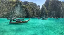 Traditional longtail boats floating in turquoise water near limestone cliffs in Phuket.