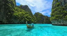 Traditional longtail boat on clear turquoise water surrounded by lush green cliffs in Phuket.