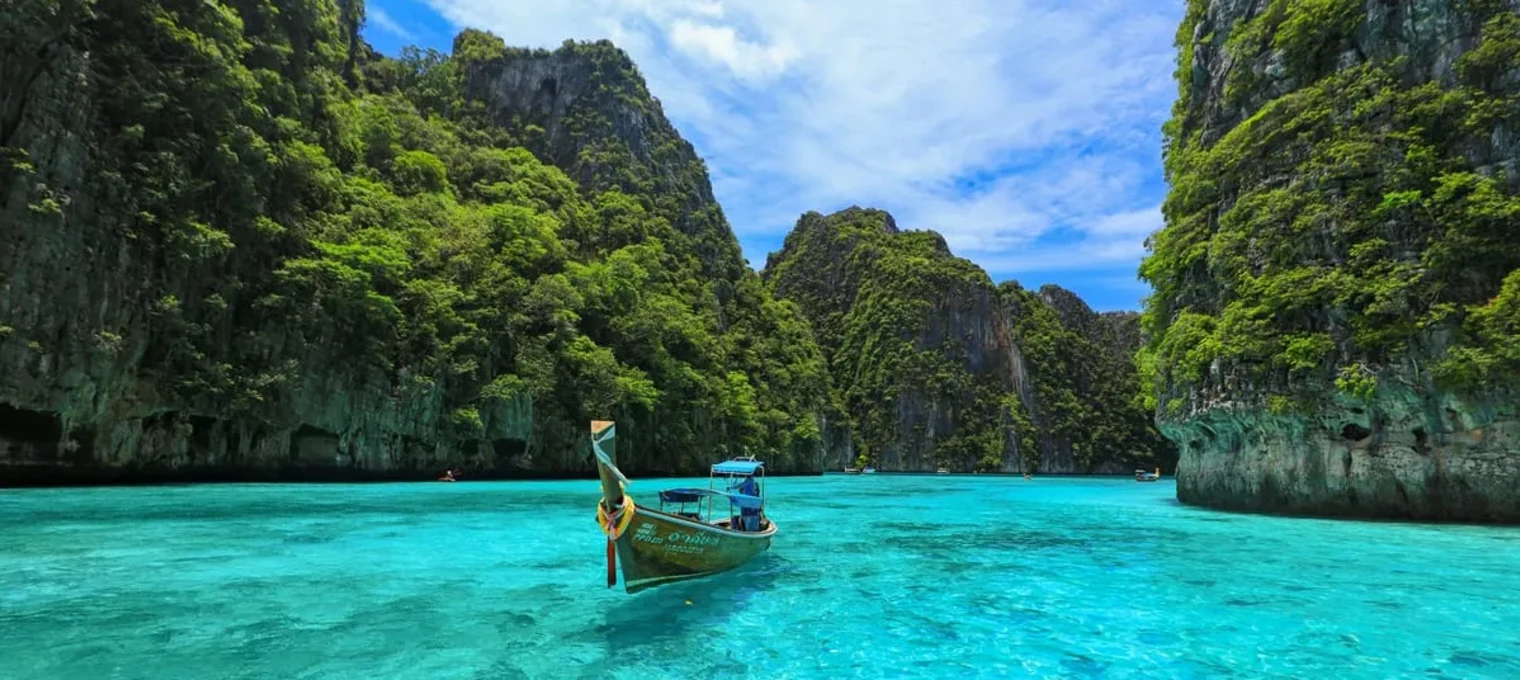 Traditional longtail boat on clear turquoise water surrounded by lush green cliffs in Phuket.