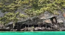 Lush green cliffs with cave openings above vibrant turquoise water in Phuket, Thailand.