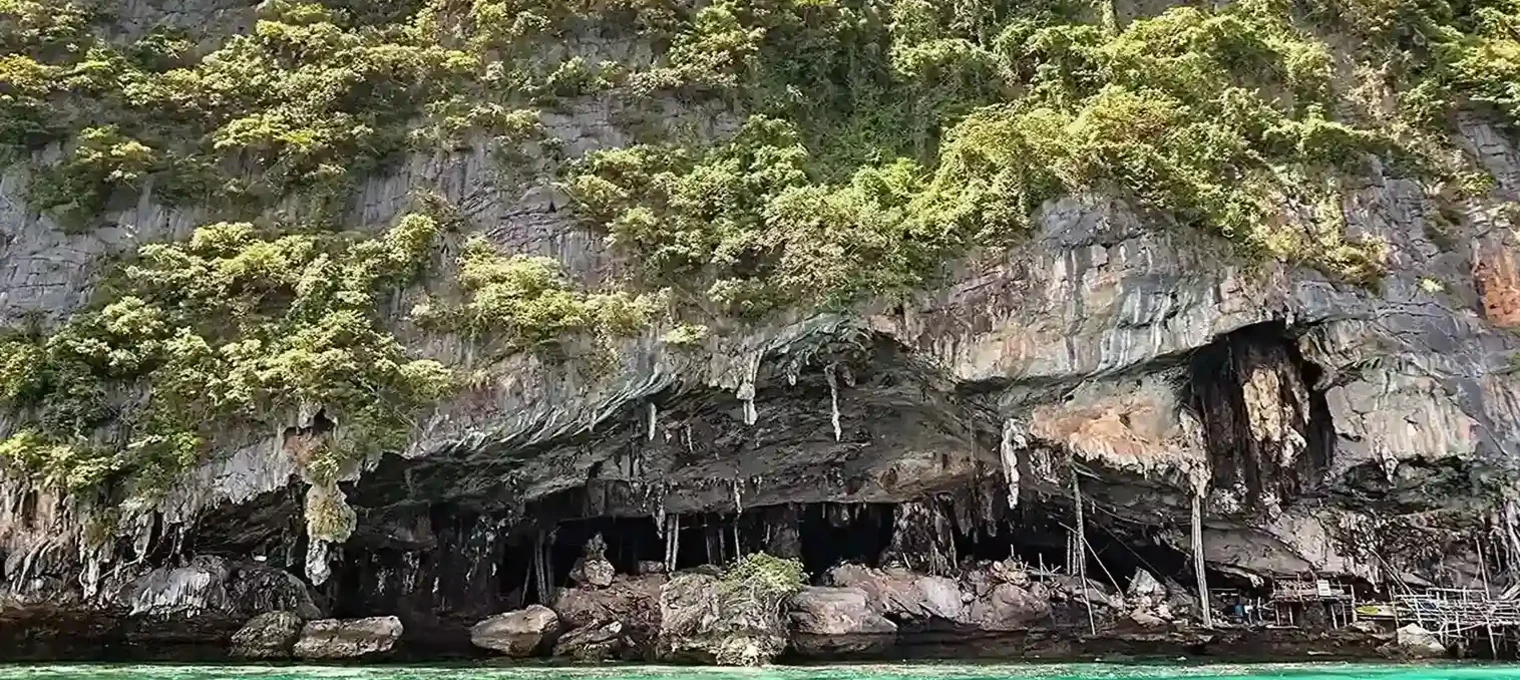 Lush green cliffs with cave openings above vibrant turquoise water in Phuket, Thailand.
