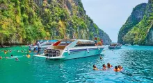 Tourists swimming near boats in turquoise waters surrounded by lush cliffs in Phuket.