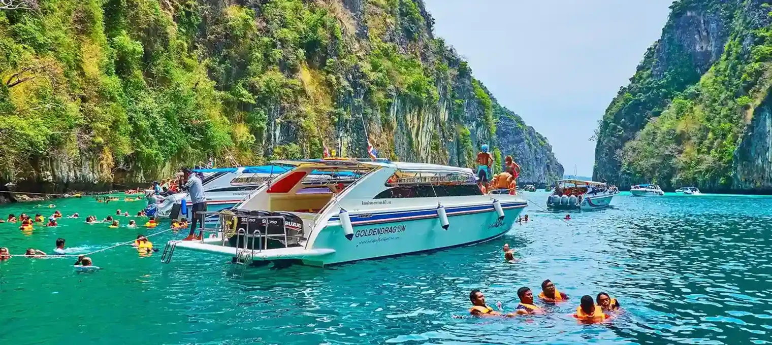 Tourists swimming near boats in turquoise waters surrounded by lush cliffs in Phuket.
