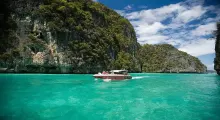 Speedboat gliding through turquoise waters near lush cliffs in Phuket, Thailand.