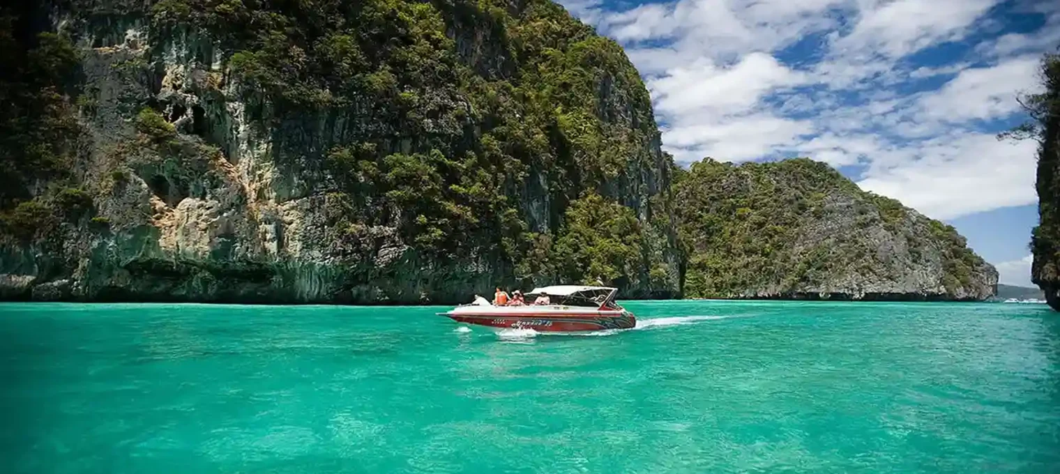 Speedboat gliding through turquoise waters near lush cliffs in Phuket, Thailand.