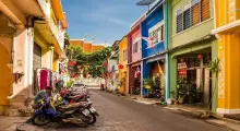 Colorful buildings line a street in Phuket, with parked motorcycles and vibrant decorations.