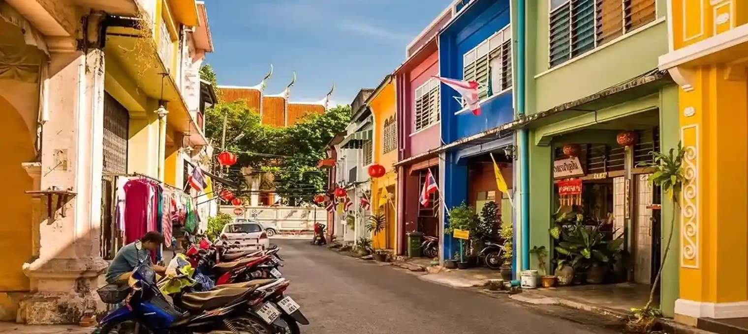 Colorful buildings line a street in Phuket, with parked motorcycles and vibrant decorations.
