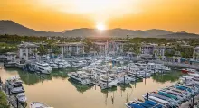 Sunset over a marina in Phuket with boats and mountains in the background.