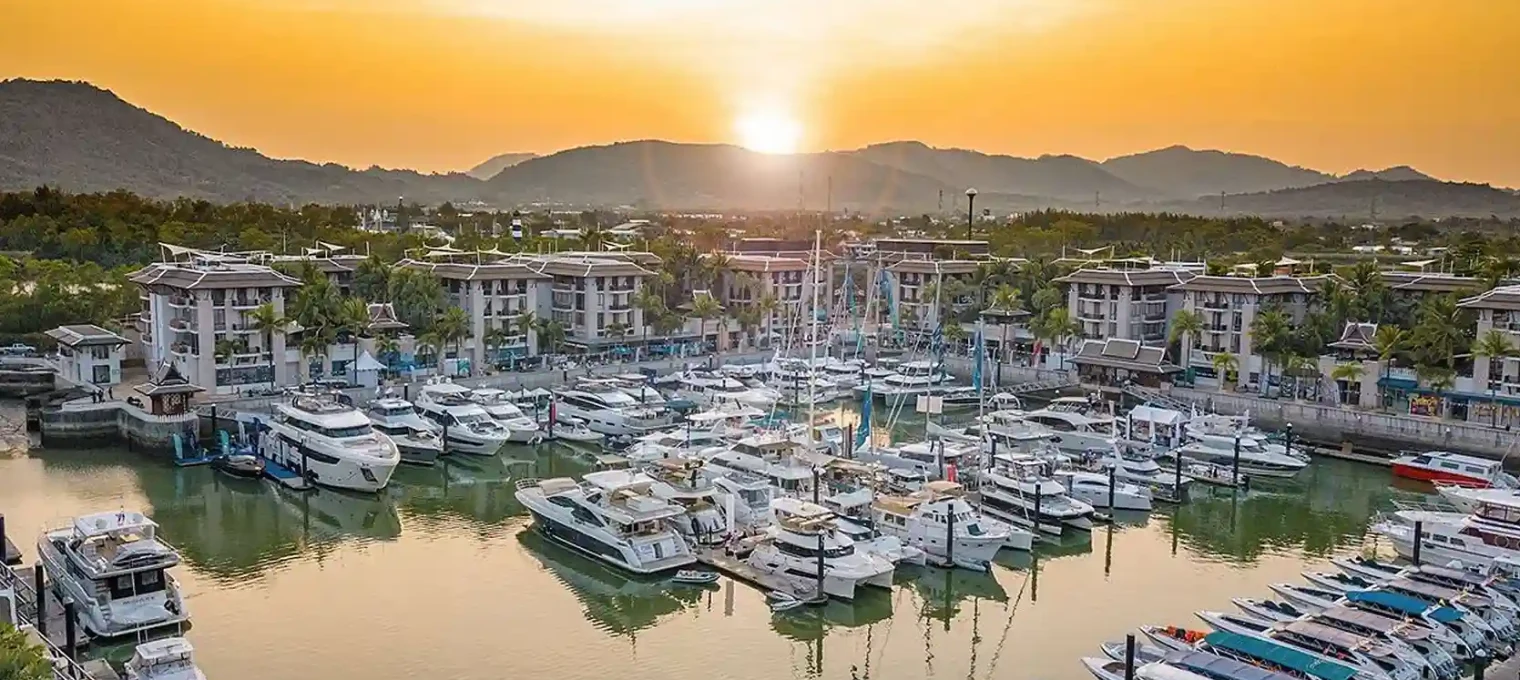 Sunset over a marina in Phuket with boats and mountains in the background.