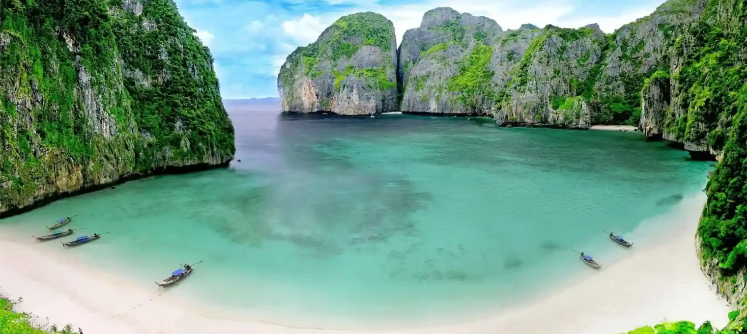 Stunning beach with turquoise water, limestone cliffs, and boats in Phuket, Thailand.