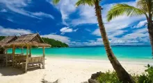 Tropical beach in Phuket with a thatched hut, palm trees, and clear turquoise water.