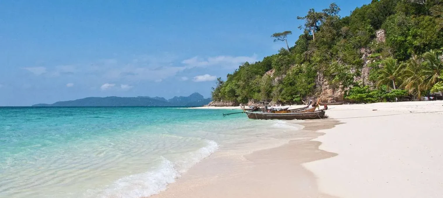 Pristine beach in Phuket with clear blue water, soft sand, and traditional fishing boats.